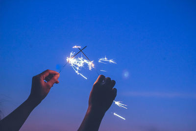 Cropped image of hands holding sparklers at night