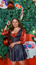 Portrait of smiling young woman standing against christmas tree