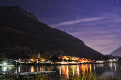 Scenic view of river by mountains against sky at night