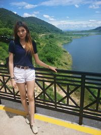 Portrait of smiling young woman standing by railing against sea