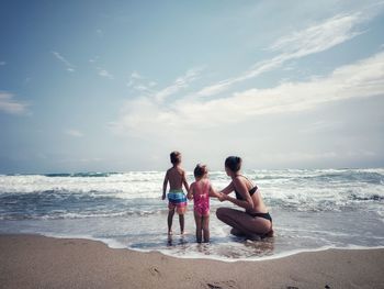 Rear view of woman sitting at beach against sky