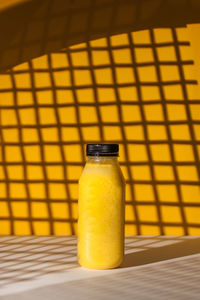 Smoothies of yellow color in a bottle on a yellow background with hard shadows. 