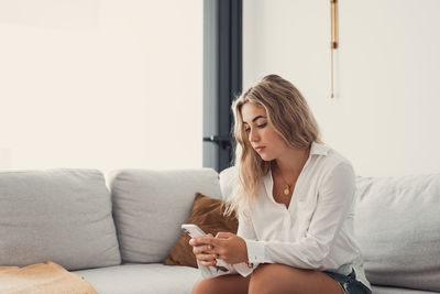 Young woman using mobile phone while sitting on bed at home