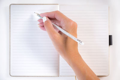 Cropped hand of woman writing in book on table