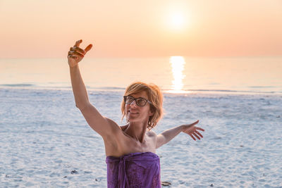 Woman with arms raised on beach against sky during sunset