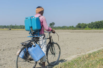 Indian farmer riding a bicycle carrying a spray machine at farm field