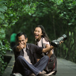 Smiling young couple sitting against trees