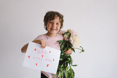 Cheerful happy child with peonys bouquet and a card for mom in ukrainian language.