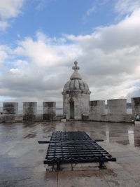 Bench in front of building against cloudy sky