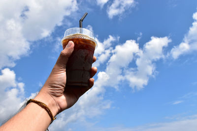 Low angle view of hand holding drink against sky