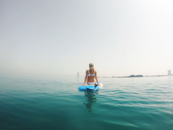 Woman sitting in sea against clear sky