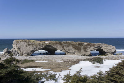 Rocks by sea against clear blue sky