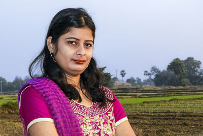 Portrait of beautiful woman standing on field against sky