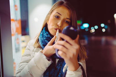 Beautiful woman applying lipstick at night