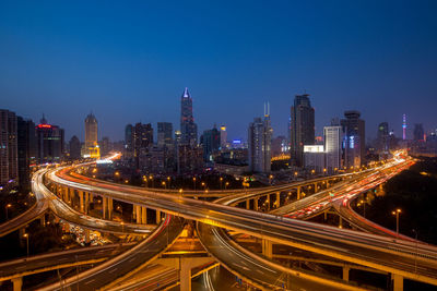 High angle view of illuminated light trails on road amidst buildings in city at night