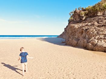 Rear view of boy running on beach against sky