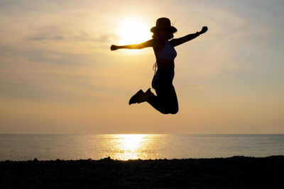 Silhouette man jumping in sea against sky during sunset