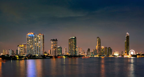 Sea by illuminated buildings against sky at night