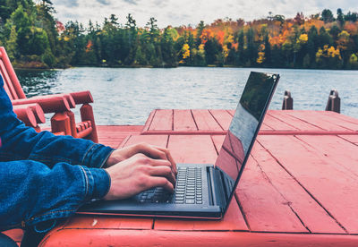 Low section of man using mobile phone while sitting by lake