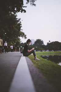 Side view point candid of young woman sitting on ground relax and play with her mobile phone