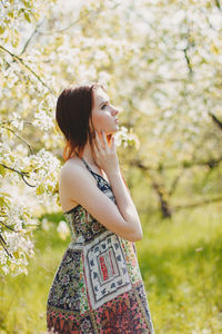 Woman with arms raised standing against tree