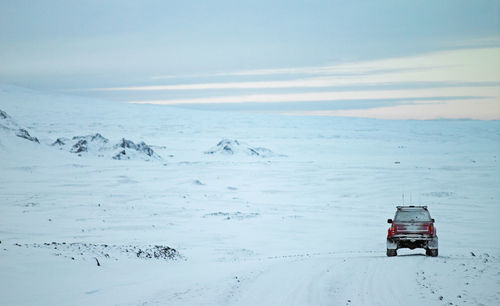 Red suv driving through winter landscape in iceland