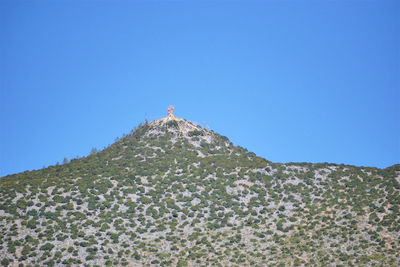 Low angle view of person on mountain against clear blue sky