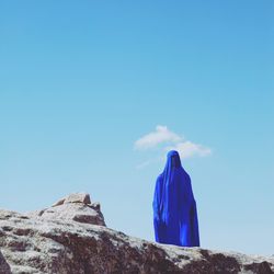 Low angle view of woman in burka standing on rock formation against blue sky during sunny day