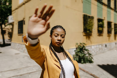 Young woman with hand raised standing in city during sunny day