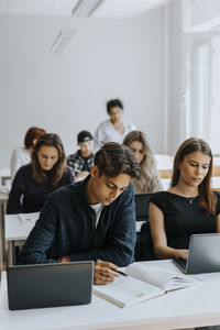 Male and female students sitting at desk while studying in classroom