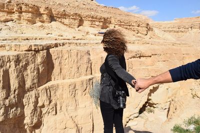 Cropped hand of man holding woman standing against rocky mountains