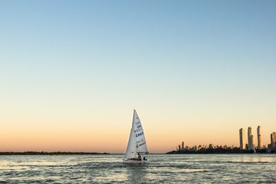 Man on sailboat sailing in sea at sunset