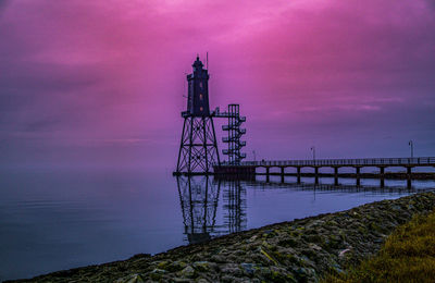 Electricity pylon by sea against sky during sunset