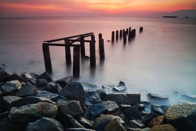 Wooden posts in sea against sky during sunset