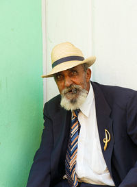 Portrait of man smoking cigar while sitting against wall