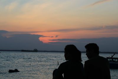 Rear view of silhouette couple at sea against sky during sunset