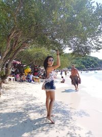 Portrait of woman standing by tree at beach