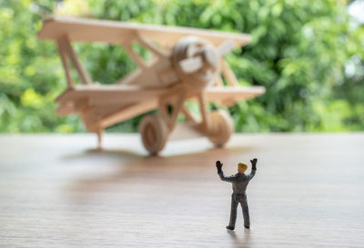 Close-up of toy airplane with figurine on wooden table against trees