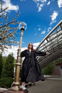 Full length of woman in oversized black dress walking to nowhere against built structure outdoors