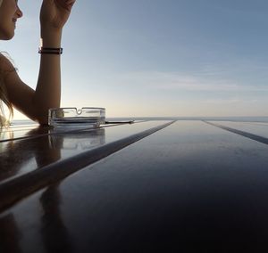 Low section of woman on table against sea during sunset