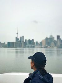 Rear view of man looking at cityscape against river