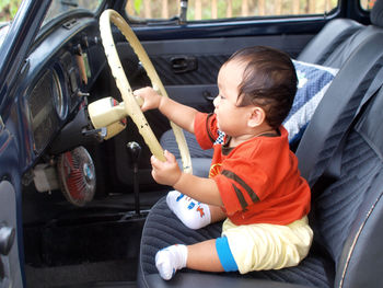 High angle view of baby boy holding a steering wheel on driver's seat of volkswagen beetle.