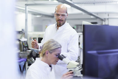 Male technician looking at female scientist doing research through microscope in laboratory