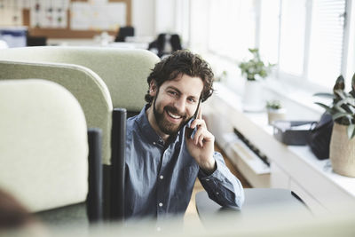 Smiling male professional talking through mobile phone while sitting on chair at creative office