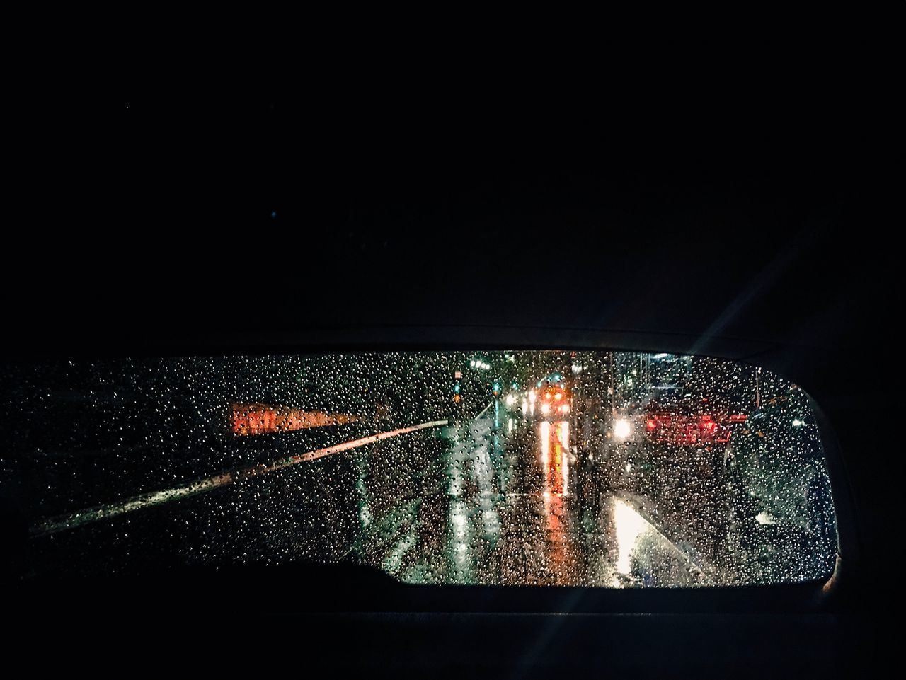 Road seen through wet rear windshield of car at night