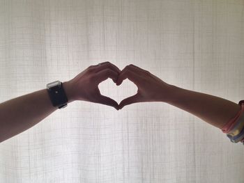 Cropped hands of couple making peace sign by curtain