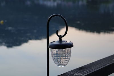 Close-up of electric lamp hanging by lake against sky