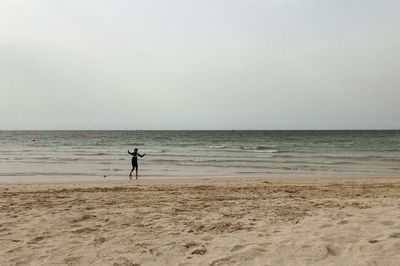 Woman running at beach against clear sky