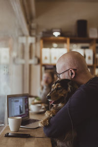 Bald man sitting with dog while using laptop at cafe