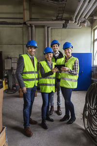 Full length portrait of confident manual workers using digital tablet in factory